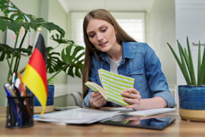 Female student looking talking to webcam, headshot portrait of young woman studying online, studying German, flag of Germany on table. E-education, e-learning, distance learning