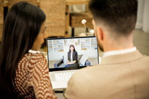 Rear view of young married couple wife and husband discussing issues and misunderstandings in relationships when having online consultation with family psychologist, sitting on sofa in livinng room